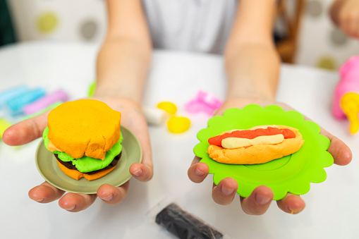 Hands presenting colorful playdough burger and hot dog