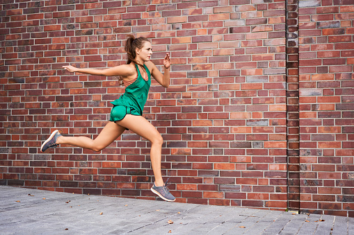 Sporty woman running jumping against brick wall in the city