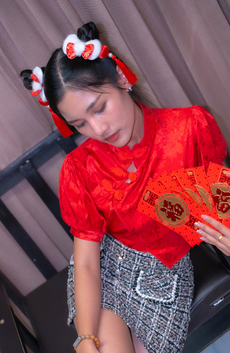 A beautiful woman with a sharp face wore a cheongsam. He was holding a red envelope and sitting on a chair. Envelopes are distributed at the festival.