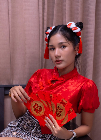 A beautiful woman with a sharp face wore a cheongsam. He was holding a red envelope and sitting on a chair. Envelopes are distributed at the festival.
