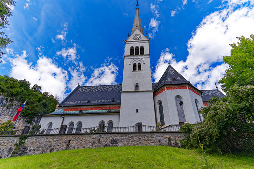 Scenic view of white St. Martin's Parish Church at lakeshore of Lake Bled on a cloudy summer day. Photo taken August 8th, 2023, Bled, Slovenia.