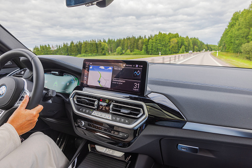Sweden. Uppsala. 08.31.2023. Woman driver operating BMW iX3-M electric car on highway outside city on summer day.