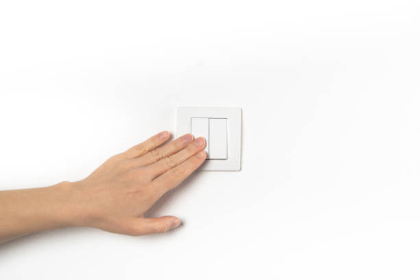 Closeup of hand and light switch. Womans hand with fingers on light switch, about to turn off the lights. Horizontal format. White wall.