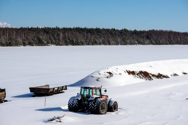 istock Red big tractor in winter on field with tree and blue sky background 2000210512