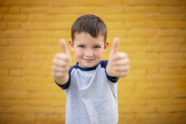 Smiling Boy Giving Thumbs Up Against Yellow Wall