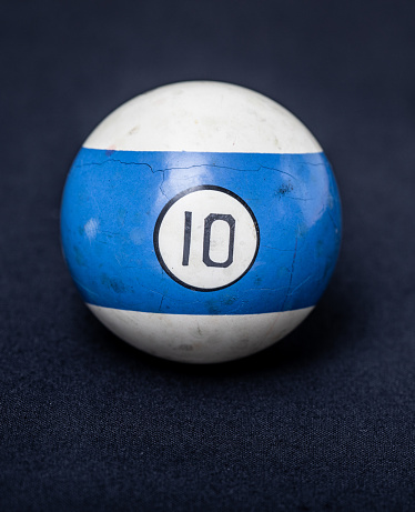 Studio shot of a worn and cracked number ten billiard ball on a simple background with blue stripe.