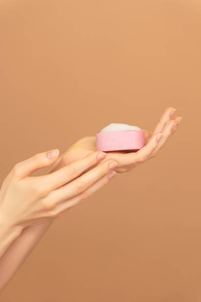 istock Close-up of female hands palm with pink solid face cleanser on peach background 2000216129