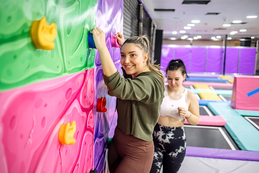 Two young women enjoying exercising in playground hanging on the free climbing wall