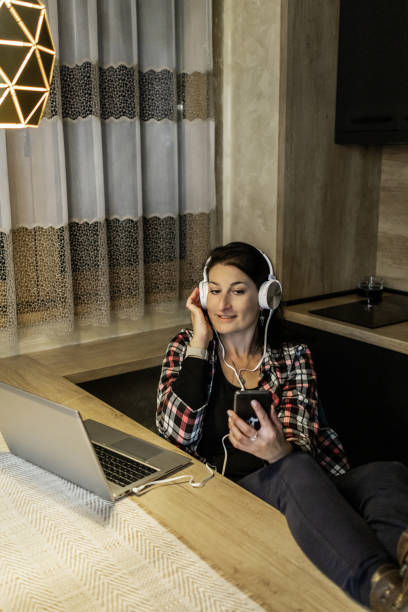 istock Beautiful mid adult woman is taking a break from working on laptop at kitchen dining table late at night and enjoying in listening to music. 2000237764