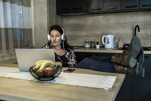 istock Beautiful mid adult woman is taking a break from working on laptop at kitchen dining table late at night and enjoying in listening to music. 2000239331