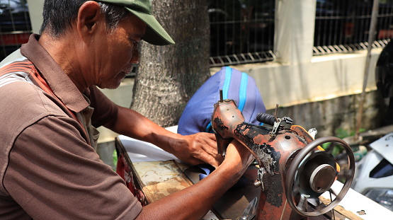Street tailor doing the order repairing bag with manual sewing machine, Pekalongan Indonesia February 6 2024