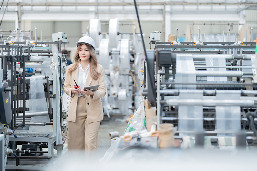 Warehouses in plastic and steel production factories Machines are producing materials for export. and the business owner is an Asian female engineer. Wear a hard hat, have a radio, laptop, suit.