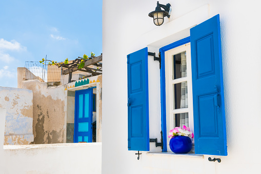Window with blue shutters and flower. White architecture in Megalochori village, Santorini island, Greece.
