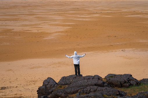 Female girl with open arms standing on rock at Rauðasandur (Red Sand) beach in Westfjords, Iceland. Beautiful endless beach with sand that changes color depending on the weather and time of day