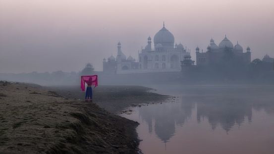 Taj Mahal in the beautiful morning sunrise and a woman is wearing Indian traditional clothes and standing by the river, Taj Mahal is the jewel of Muslims art in India and one of the universally admired masterpieces of the world's Heritage.