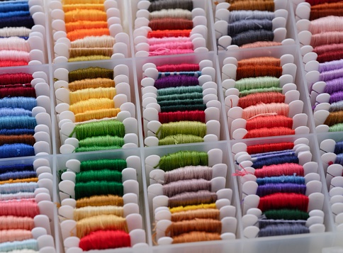 Plastic sorting box full of bobbins with different colour embroidery threads.