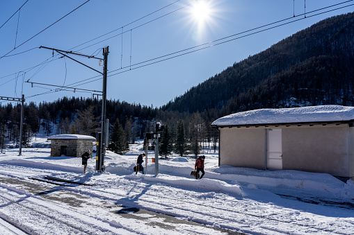 switzerland, 01/13/2024Three people walk alongside the tracks of a small train station high in the mountains covered by snow glistening in the sunshine