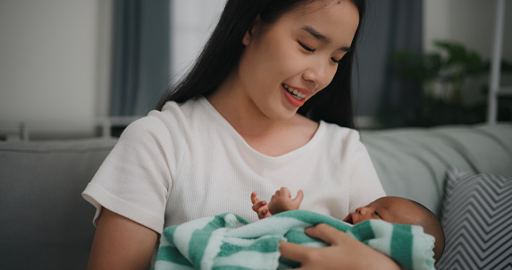 Young asian mother smile with happiness while holding newborn baby in arms Rocking and sing lullabies to put her baby to sleep at home