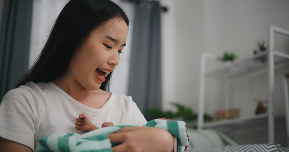 Young asian mother smile with happiness while holding newborn baby in arms Rocking and sing lullabies to put her baby to sleep at home