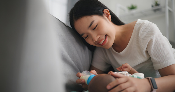 Newborn wake up and Young asian mother feeding her baby with a bottle, happily smiling and touching her baby.