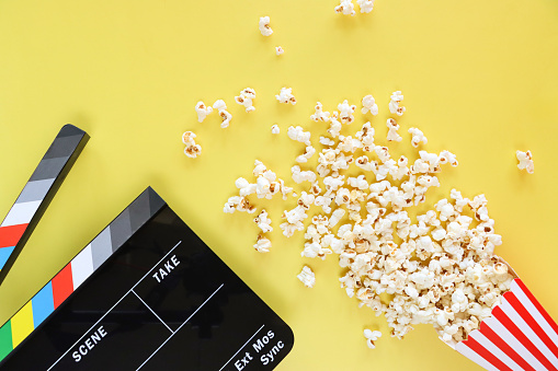 Stock photo showing close-up view of film slate and popcorn in a red and white striped cardboard carton a popular snack eaten in movie theatre cinemas.