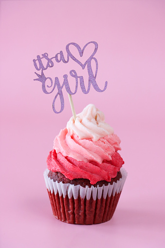 Stock photo showing close-up view of a single freshly baked, homemade, red velvet cupcake in paper cake case. The cup cake has been decorated with a swirl of ombre effect pink piped icing.