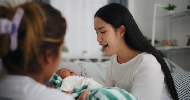 grand-mère ou nounou aide une jeune mère à porter un nouveau-né - baby yawning asian ethnicity newborn photos et images de collection