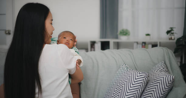 young asian mother carrying newborn on shoulder and talking with baby - baby yawning asian ethnicity newborn photos et images de collection