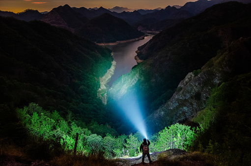 A person holding a flashlight is lighting on the mountaintop