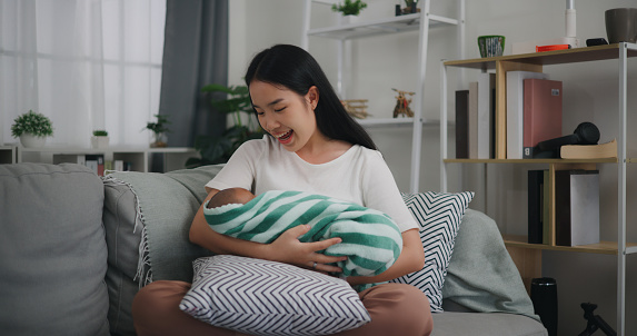 Portrait Young asian mother holding her newborn in arms, Innocence infant in blanket waking up, she talking with her baby with love