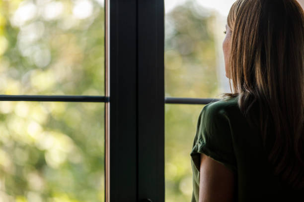 istock Woman standing by the window, looking outside, contemplating 2000364258