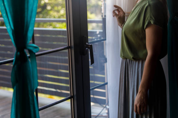 istock Woman standing by the window, looking outside, contemplating 2000364264