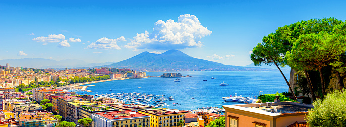 Naples, Italy. View of the Gulf of Naples from the Posillipo hill with Mount Vesuvius far in the background and some pine trees in foreground. Banner header horizontal image.