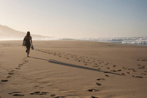 istock Woman walking on the beach leaving footprints in the sand 2000403449