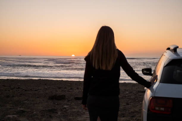 istock Woman leaning against the car watching the sunset 2000405582