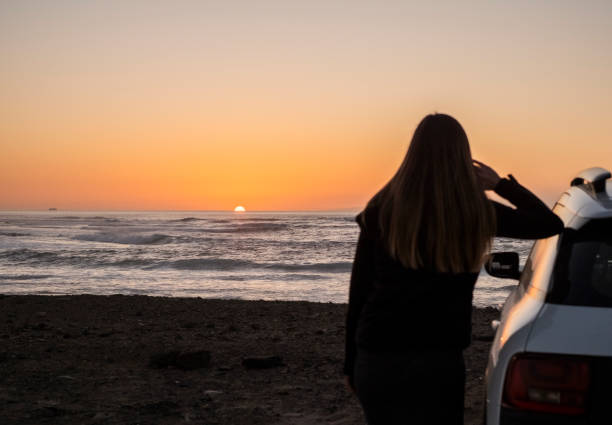 istock Woman leaning against the car watching the sunset 2000405588