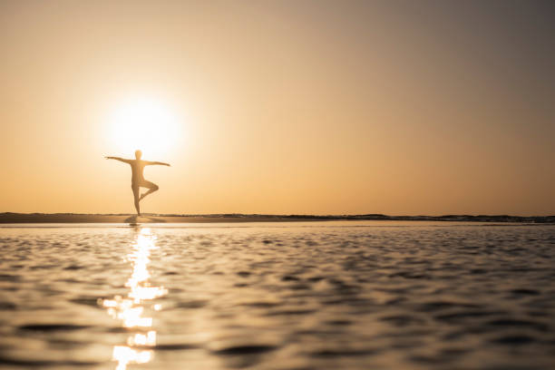 A woman, immersed in the serenity of dawn, as she engages in refreshing stretches on the tranquil beach. The gentle morning waves and the warm hues of the sunrise create a perfect backdrop for a moment of rejuvenation and self-care