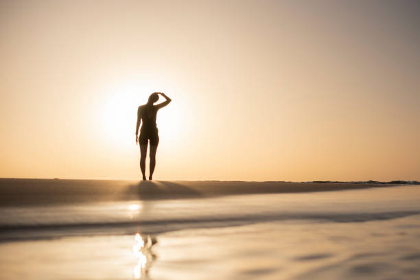 A woman, immersed in the serenity of dawn, as she engages in refreshing stretches on the tranquil beach. The gentle morning waves and the warm hues of the sunrise create a perfect backdrop for a moment of rejuvenation and self-care
