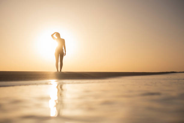 A woman, immersed in the serenity of dawn, as she engages in refreshing stretches on the tranquil beach. The gentle morning waves and the warm hues of the sunrise create a perfect backdrop for a moment of rejuvenation and self-care