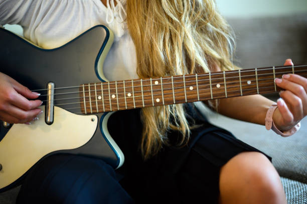 istock Young woman playing a guitare sitting on her sofa at home 2000415134