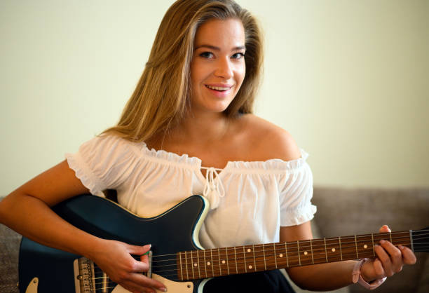 istock Young woman playing a guitare sitting on her sofa at home 2000417737