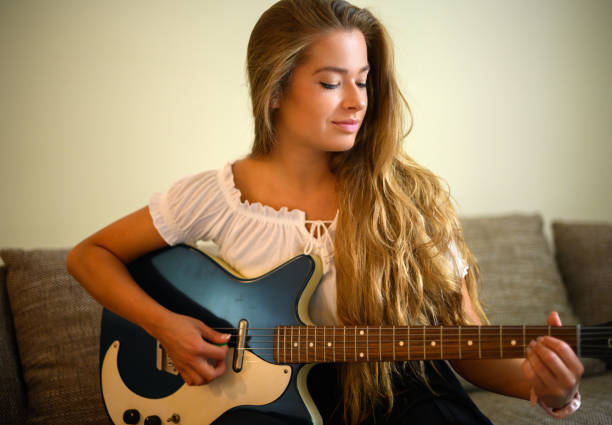 istock Young woman playing a guitare sitting on her sofa at home 2000417739