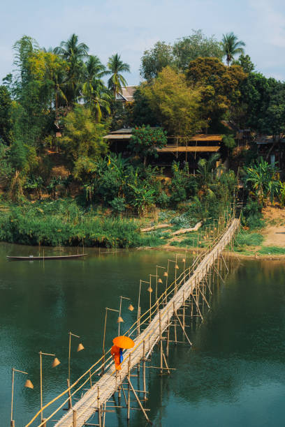 Monk in orange clothes walking over the bridge on Mekong river