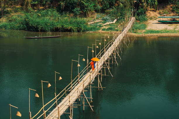 Monk in orange clothes walking over the bridge on Mekong river