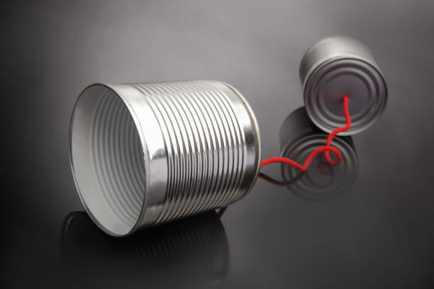 Two tin cans connected by a string are arranged to form a heart shape on a bright blue background, symbolizing love and connection through communication.