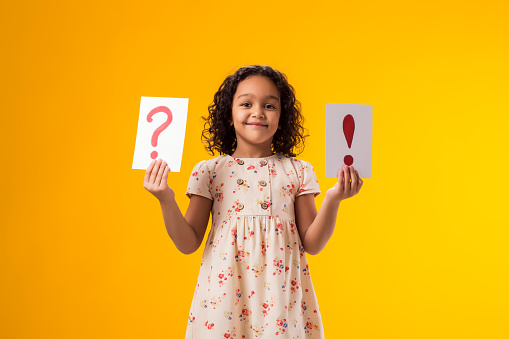 A portrait of smiling kid girl holding cards with question mark and exclamation point. Children, idea and knowledge concept