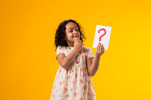 A portrait of thoughtful kid girl holding question mark card. Children, idea and knowledge concept
