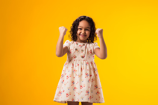Portrait of kid girl showing winner gesture over yellow background. Success and victory concept