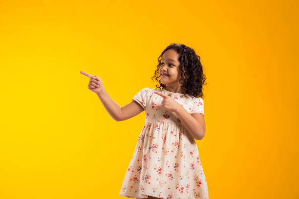 istock Smiling child girl pointing to an empty place on yellow background. Advertisement concept 2000436507