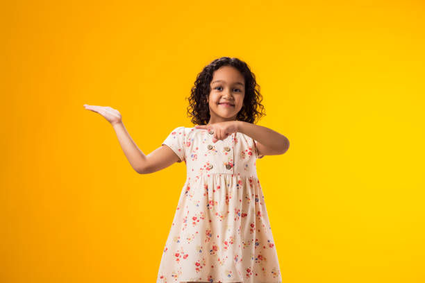 istock Smiling child girl pointing to an empty place on yellow background. Advertisement concept 2000436517